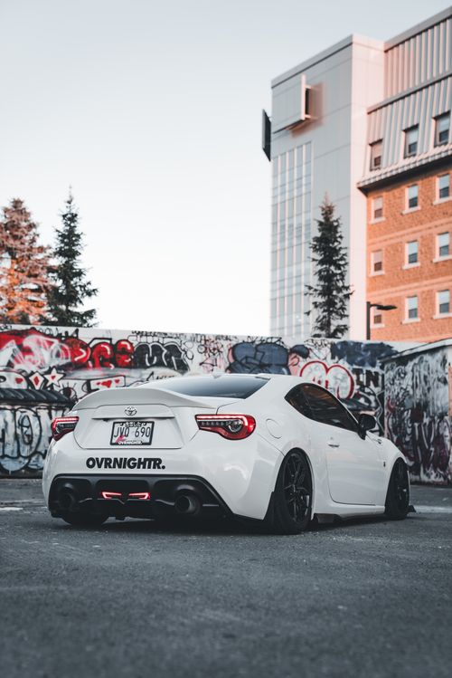 Free A sleek white sports car parked in an urban area with graffiti-covered walls, offering a modern and vibrant feel. Stock Photo