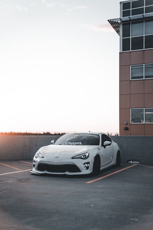 Free White sports car parked in a city lot at sunset, showcasing modern architecture and minimalistic design. Stock Photo