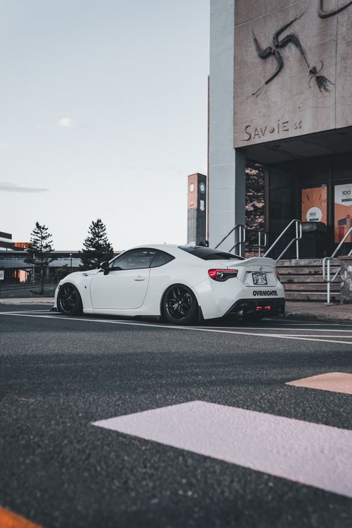 Free Modern white sports car parked outdoors near a city building with minimal traffic. Stock Photo