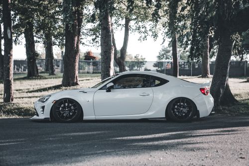 Free A white sports car parked beneath trees, casting cool shadows on a sunny day. Stock Photo