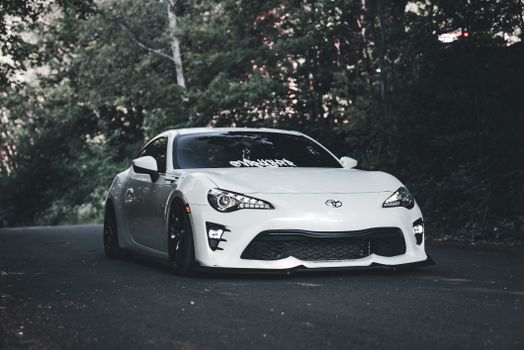 White sports car parked on a quiet forest road, blending elegance and power.
