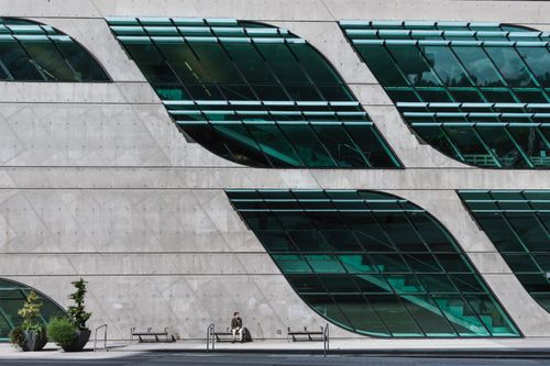 Free Contemporary building facade with unique glass window design and a lone person in urban setting. Stock Photo