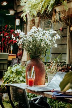 Outdoor workspace with daisies, iced drink, and laptop on rustic table.
