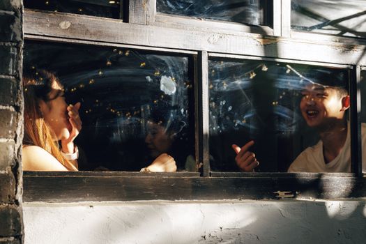 Two young adults engaging in a lively conversation through a window, creating a warm atmosphere.