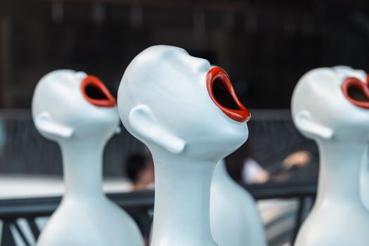 Close-up of expressive white sculptures with red mouths, capturing abstract art in daylight.