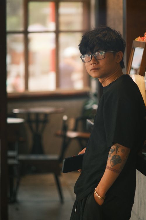 Free Young man with glasses in casual attire inside a cozy cafe, showing a contemplative mood. Stock Photo
