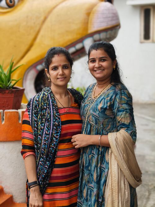Free Two women smiling in traditional attire outdoors with a colorful backdrop. Stock Photo