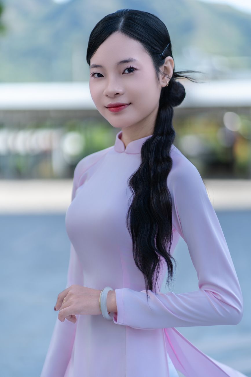 Portrait of an elegant woman in a pink Ao Dai, captured outdoors with a soft blurry background.