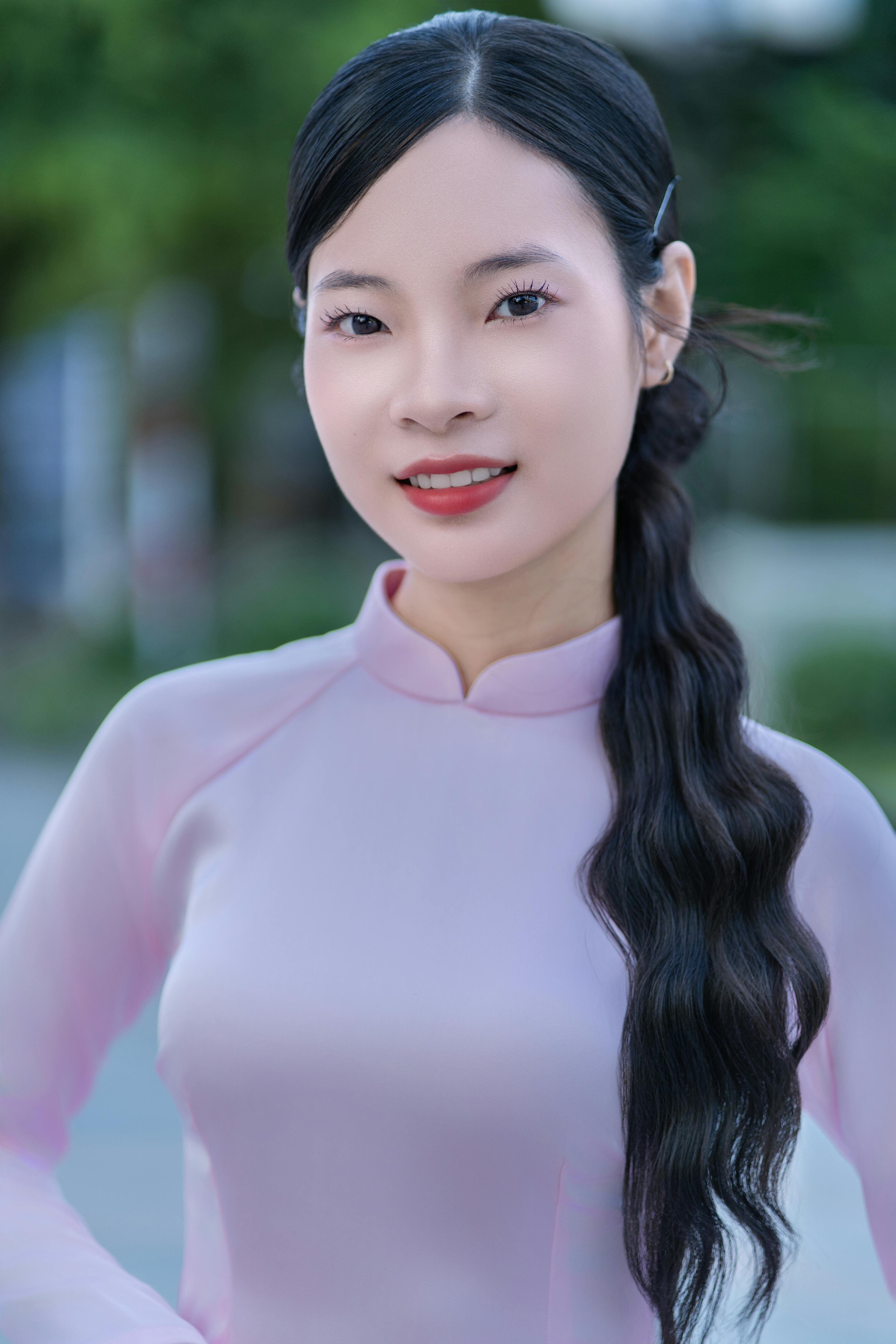 Portrait of a woman in a pink traditional dress with long, wavy hair, smiling outdoors.