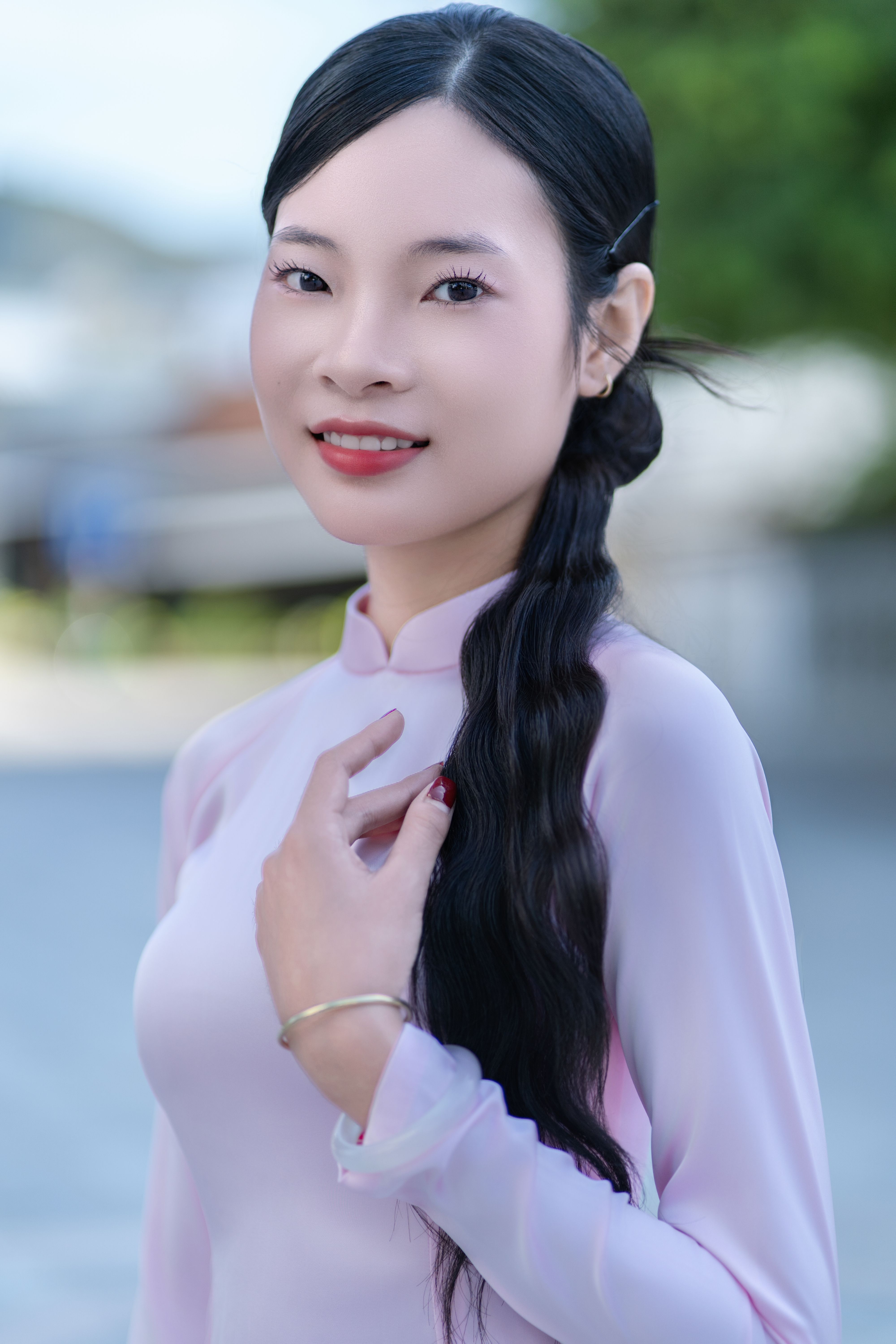 Elegant woman in traditional pink Ao Dai outdoors, smiling confidently with a serene backdrop.