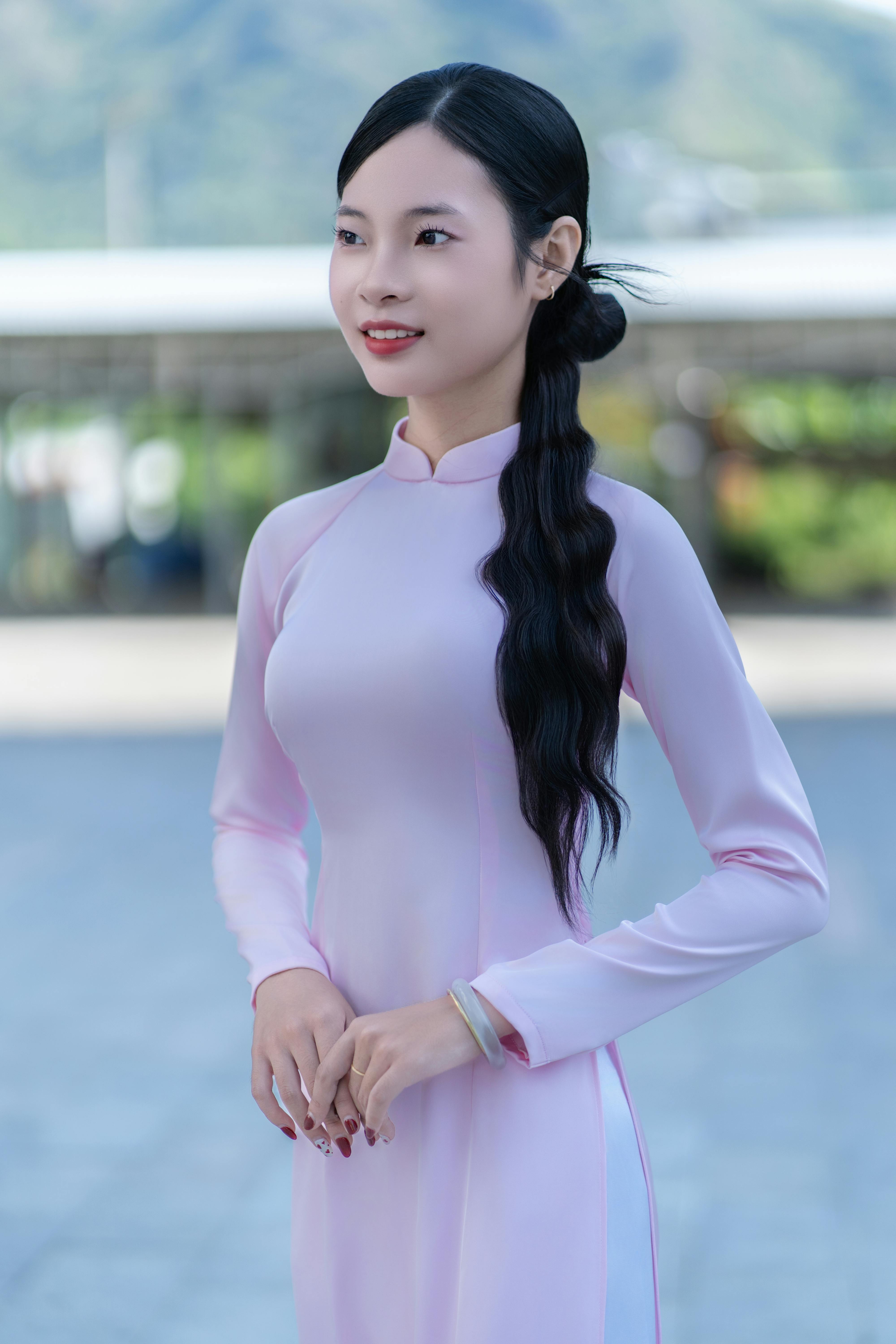 A young woman wearing a pink áo dài standing outdoors, exuding elegance and poise.