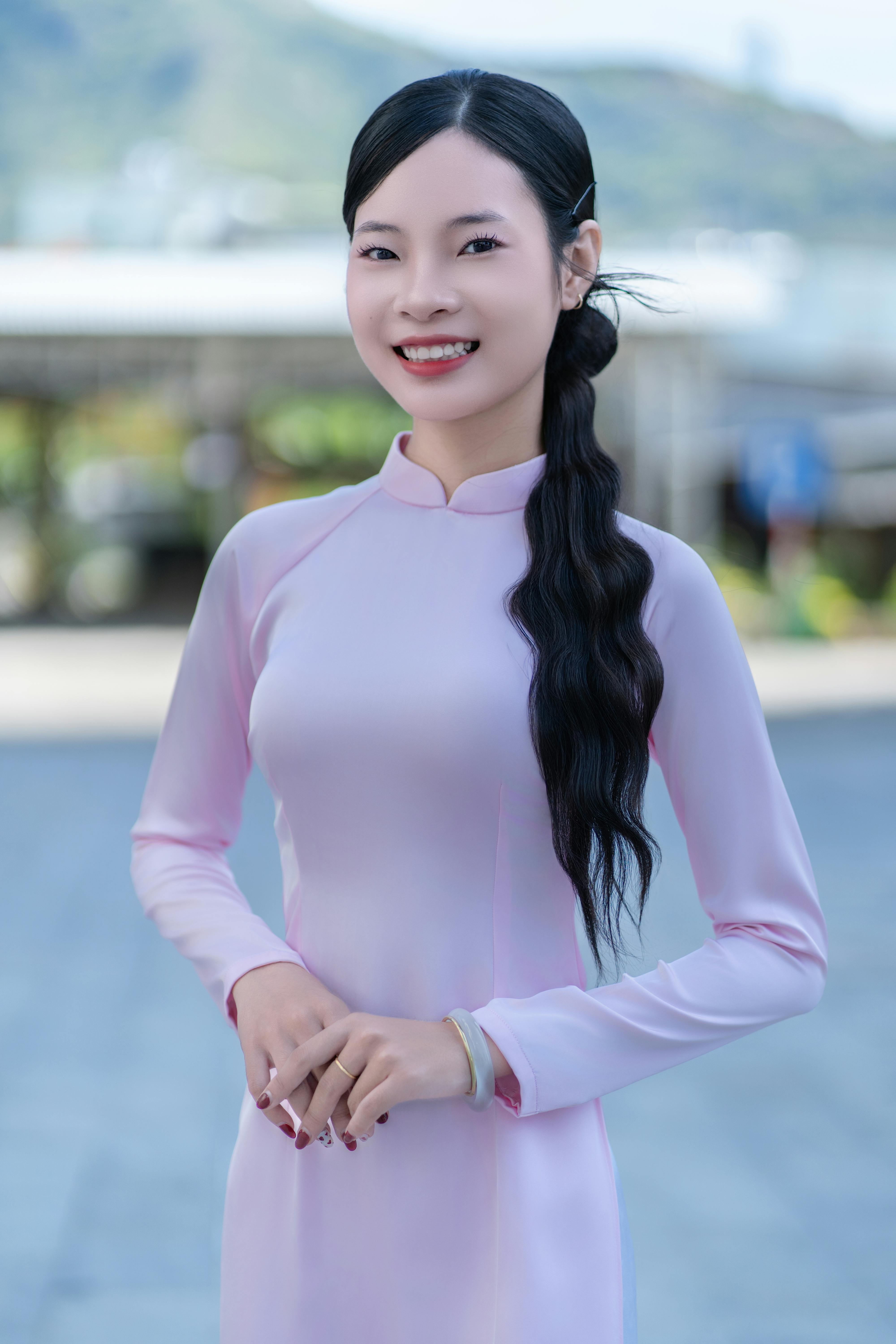 Portrait of a smiling woman wearing a pink Ao Dai dress outdoors, exuding elegance and grace.