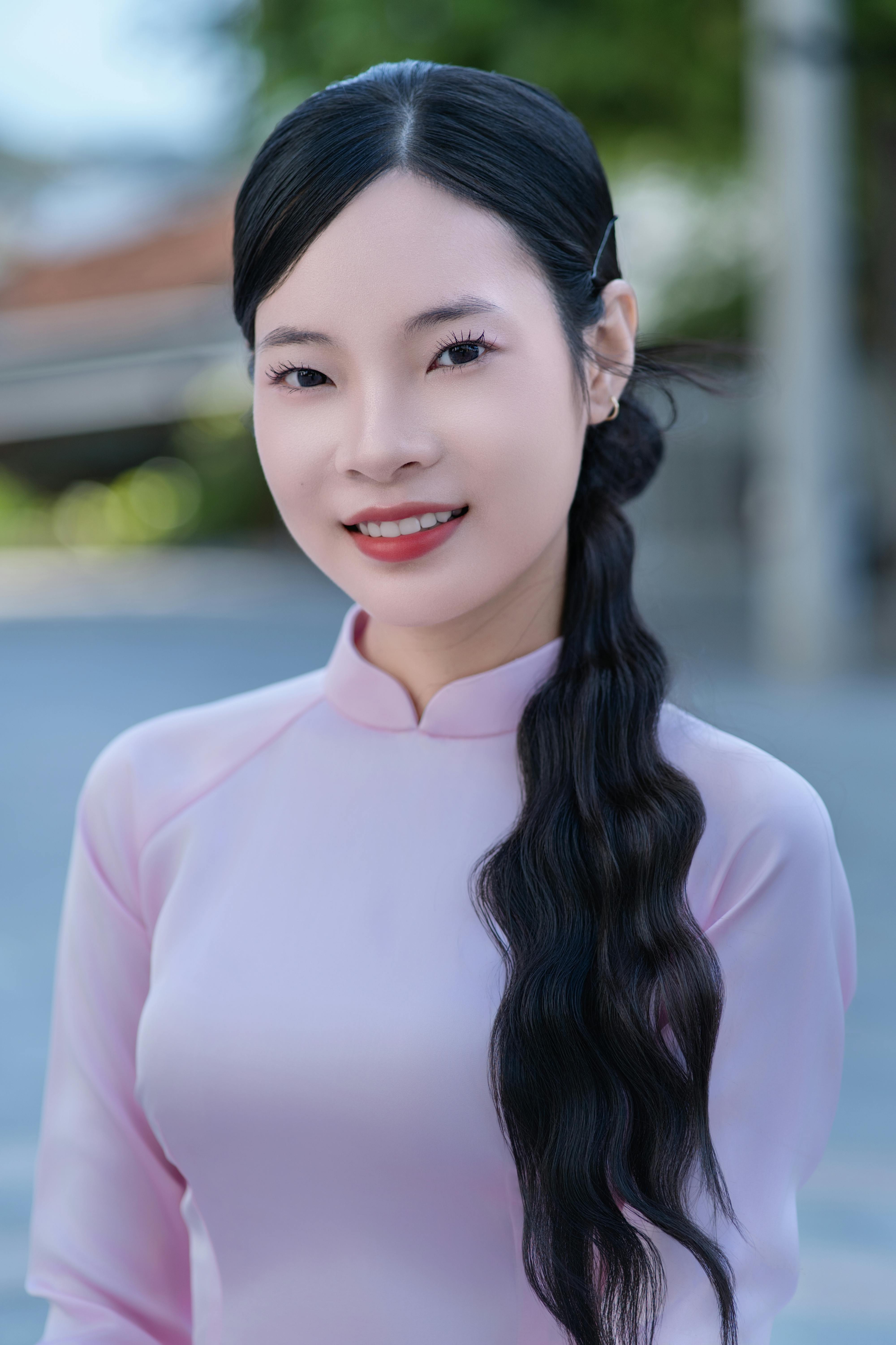 Portrait of a smiling woman in a pink dress outdoors with a vibrant background, exuding elegance and tradition.