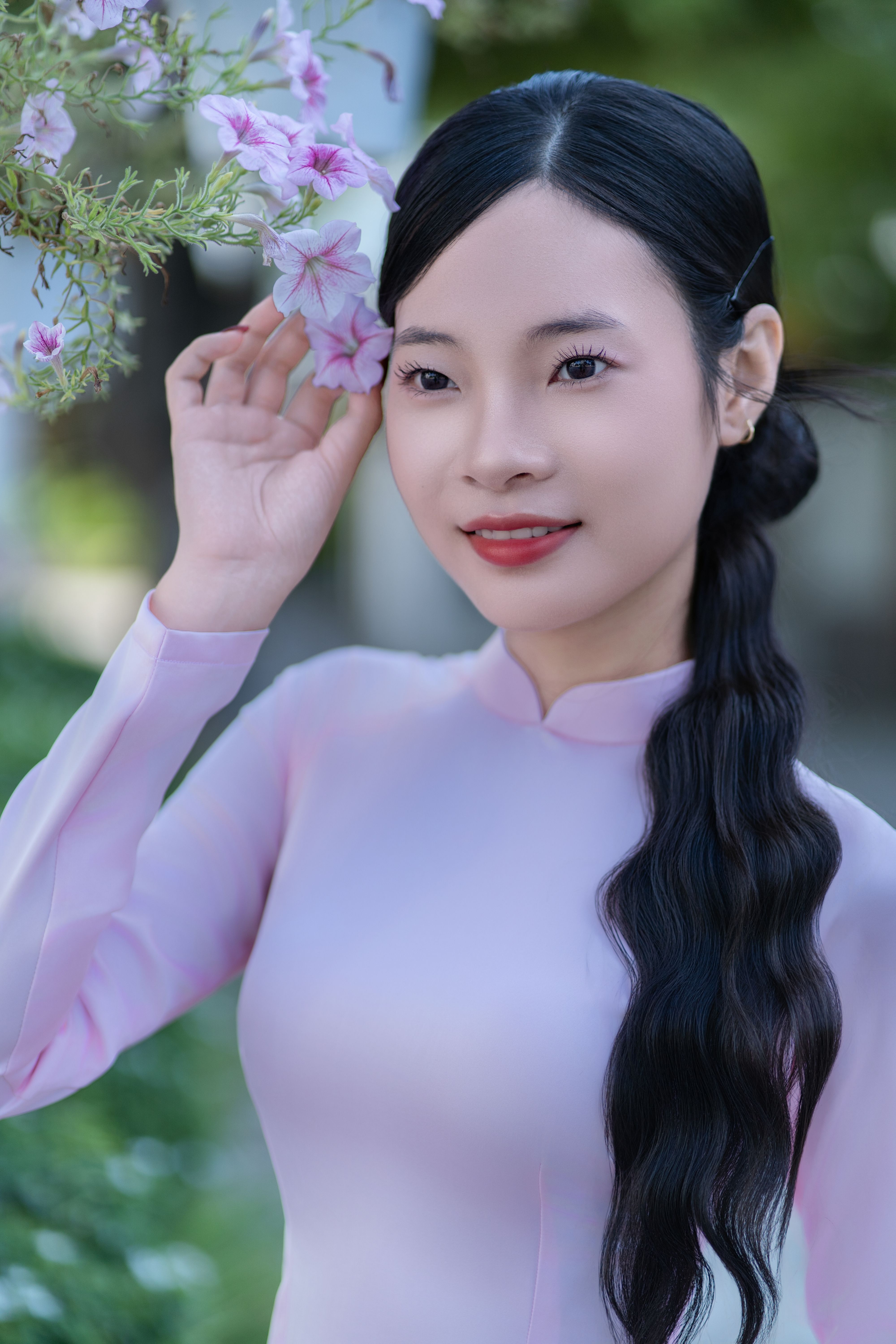 Elegant woman in traditional pink dress holding flowers, outdoors.
