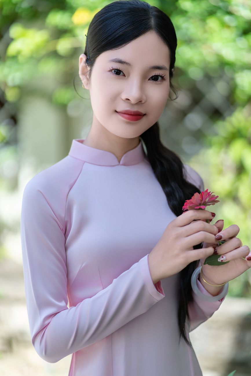Portrait of an elegant woman in traditional dress holding a small flower outdoors.