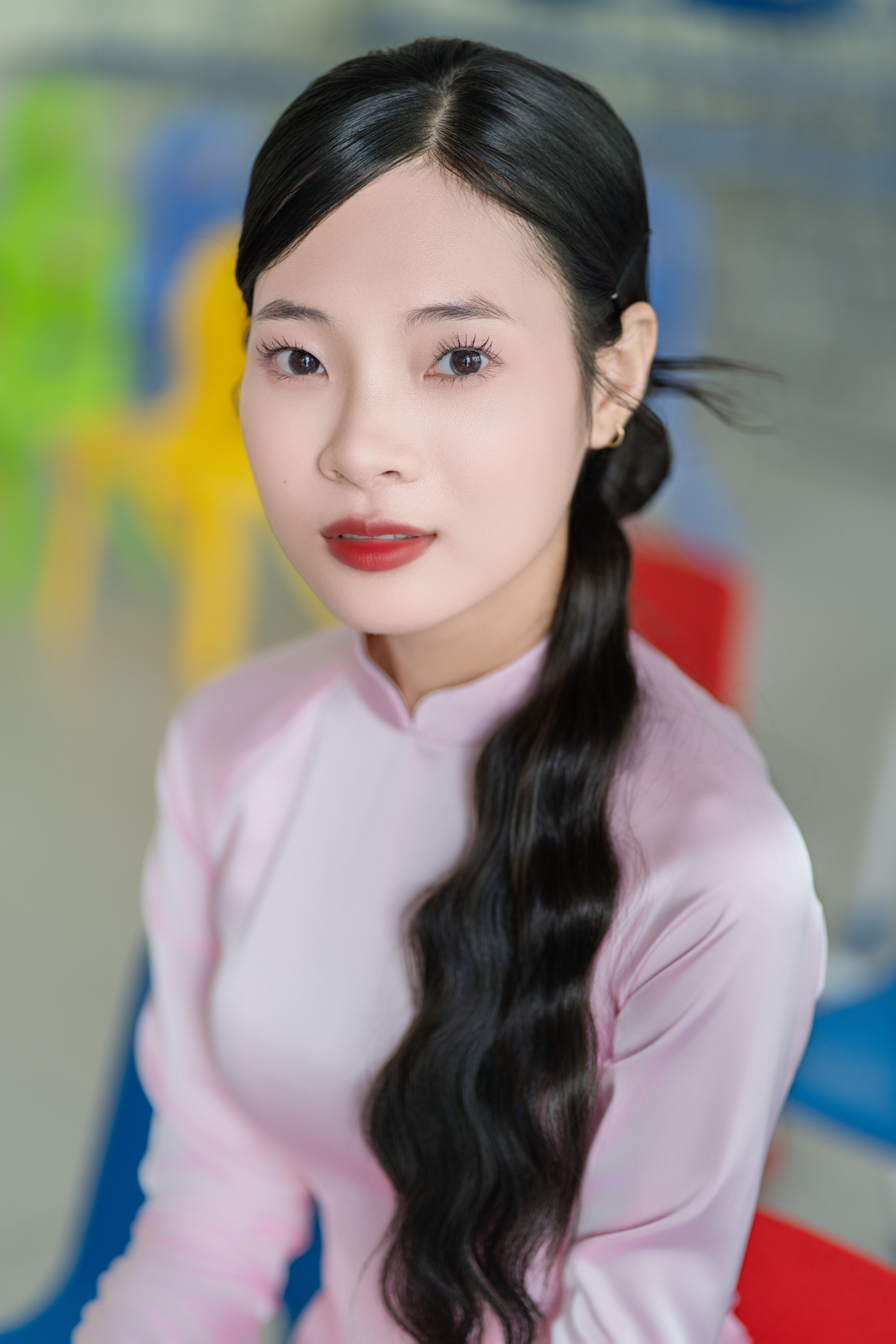 Portrait of a woman in pink traditional dress with colorful chairs in the background.