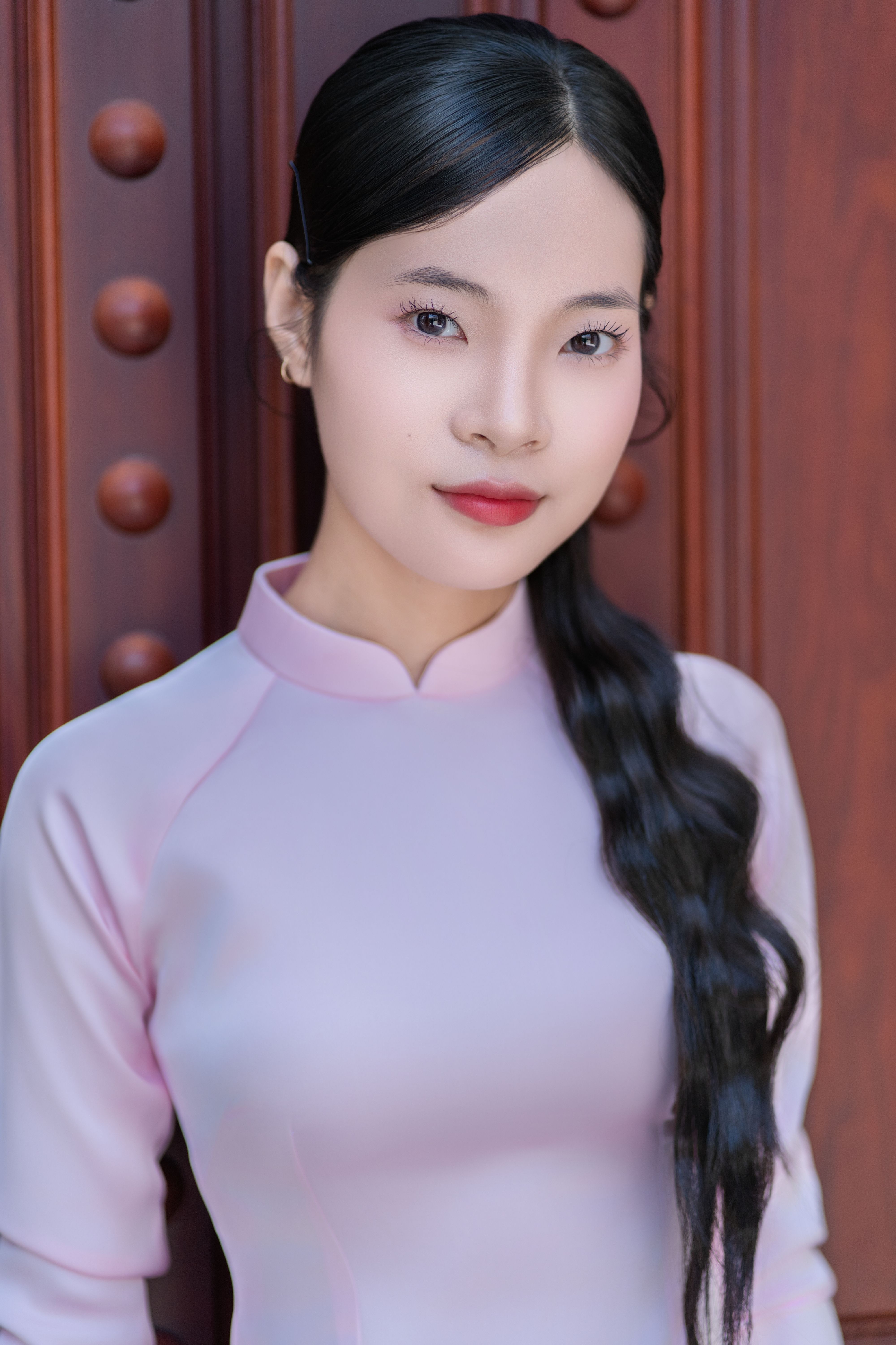 Portrait of a woman in elegant traditional dress against ornate wooden background.