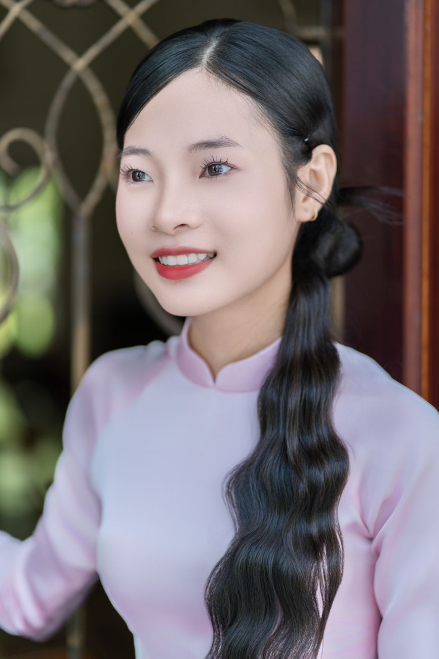 A woman in a traditional Vietnamese dress smiles gracefully indoors.