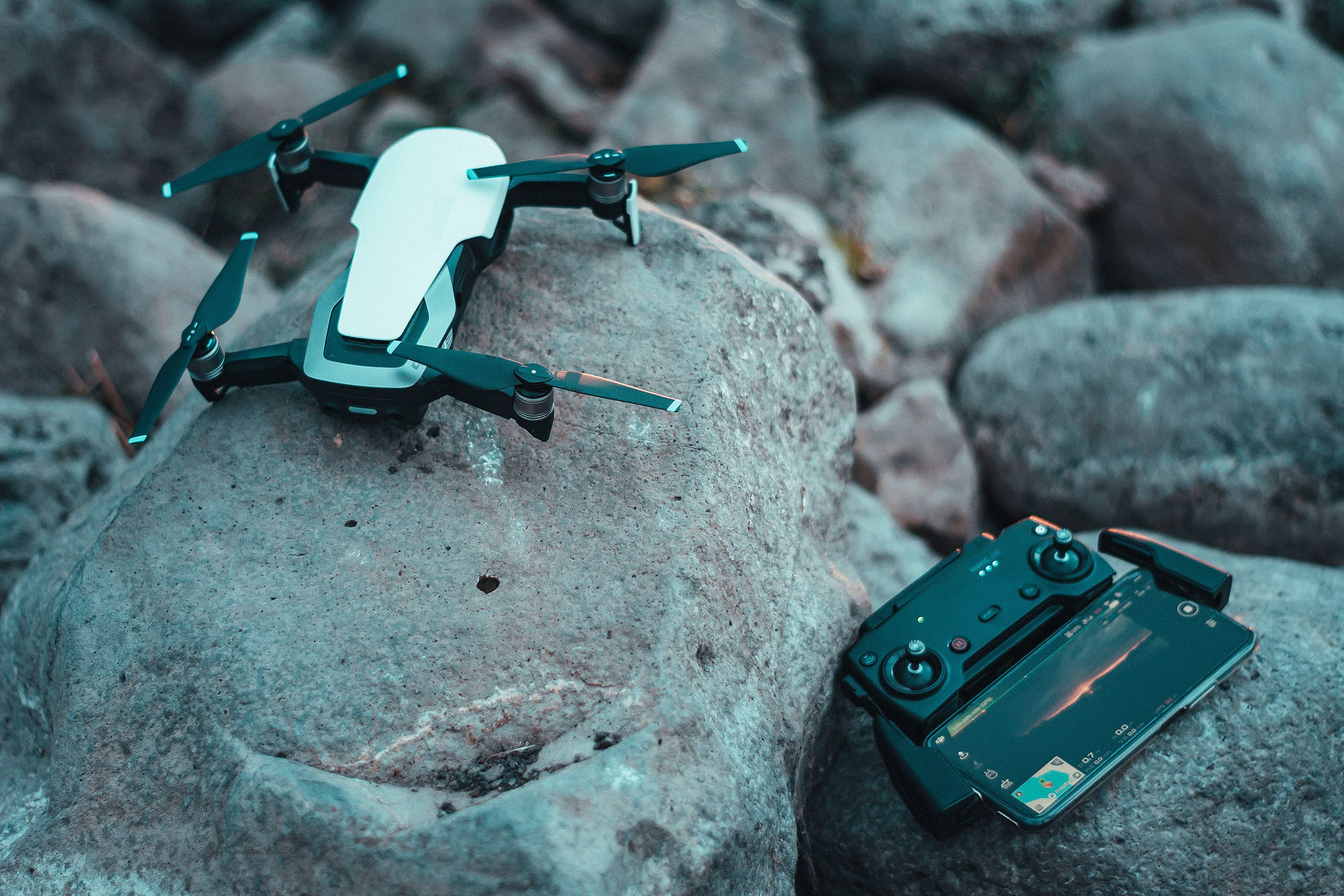 Compact drone with controller placed on rocky terrain, ready for flight in an outdoor setting.
