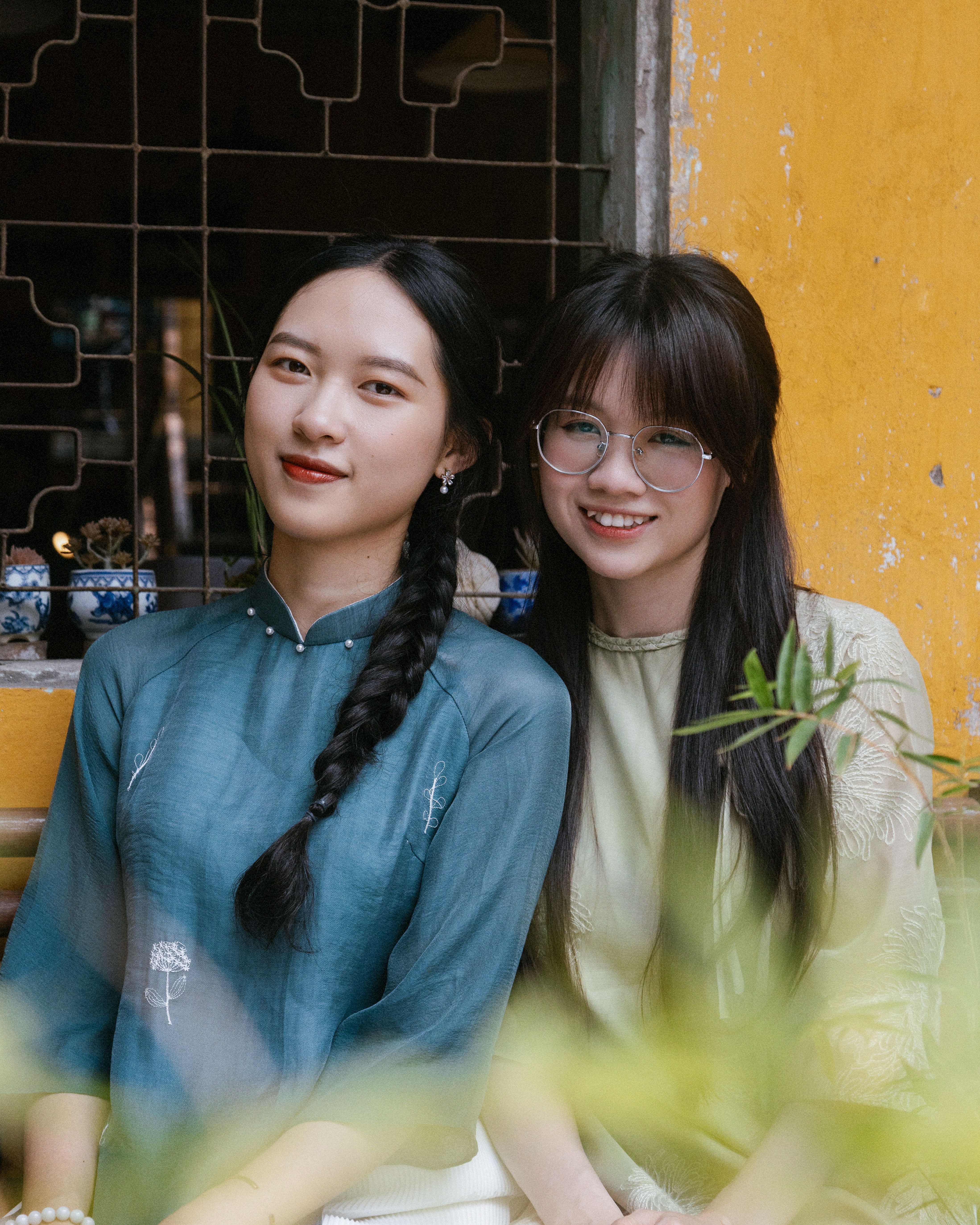 Two young women smiling and posing together by a colorful yellow wall indoors.