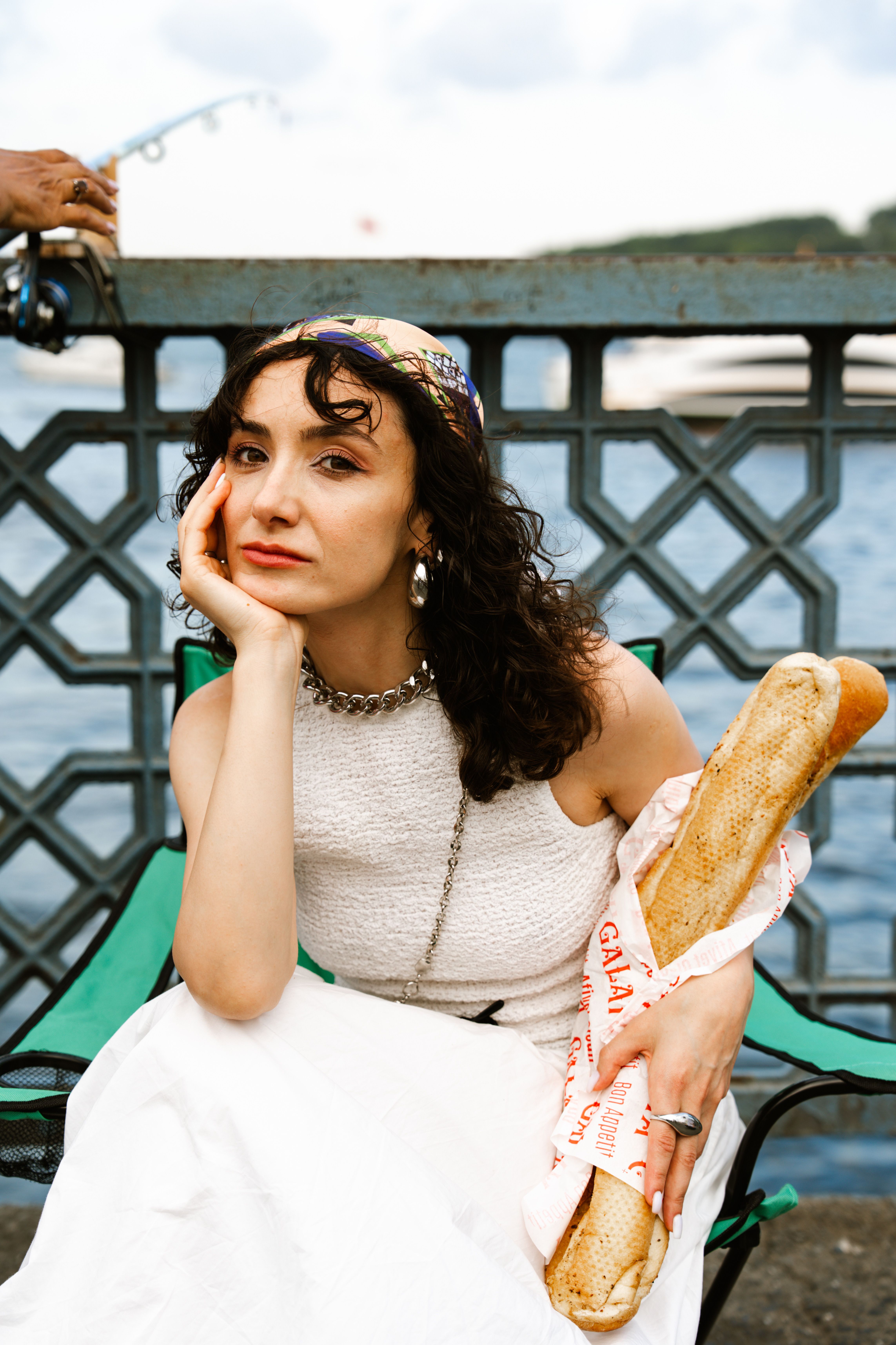 Woman in white dress with baguette sitting near water, reflecting a European vibe.