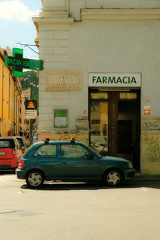Urban street view featuring a parked car and pharmacy in daylight.