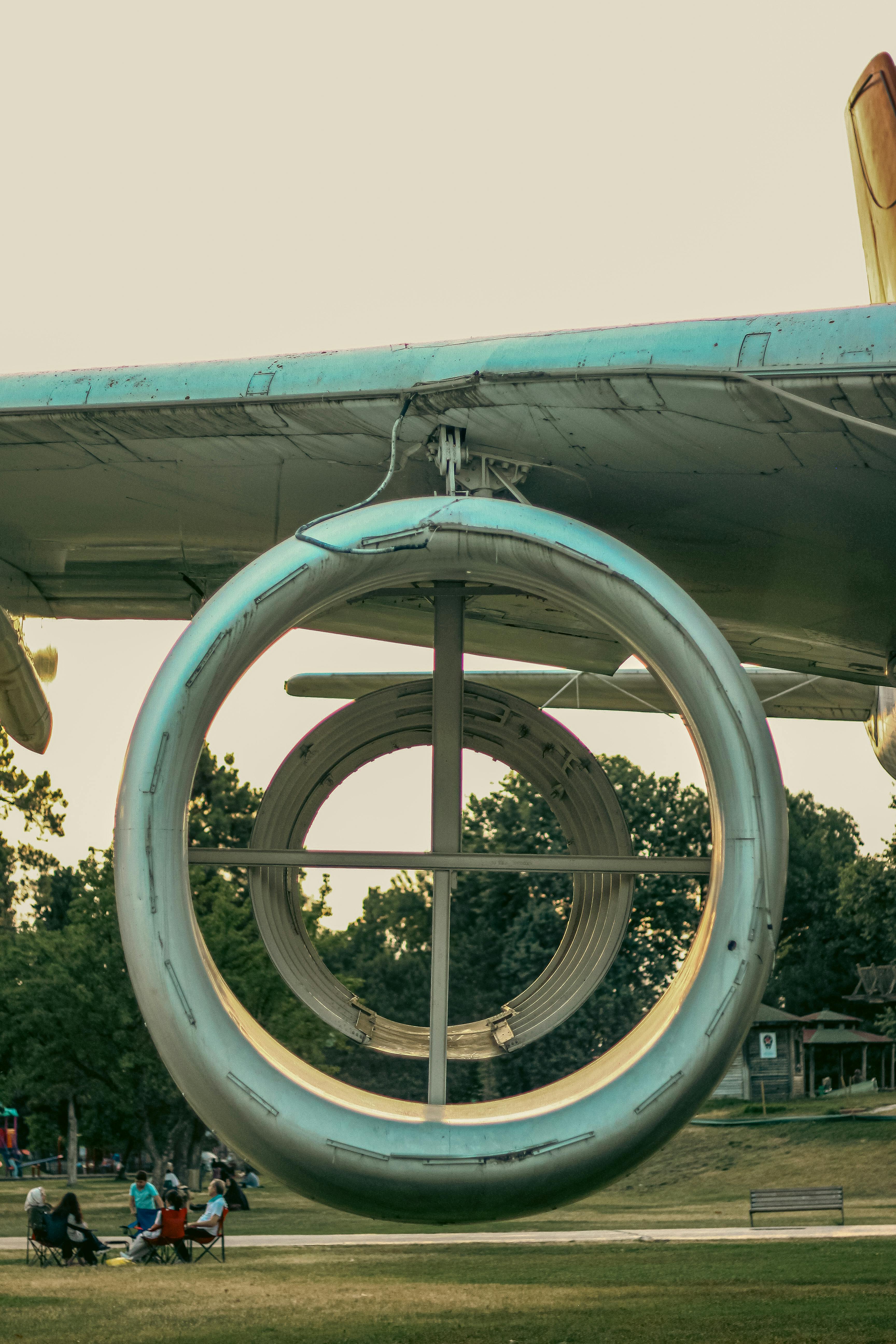 Close-up of vintage airplane engine and families enjoying a sunny day in a park.