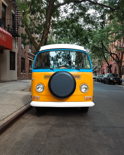 Free Front view of a vibrant classic VW van parked on a tree-lined street in NYC. Stock Photo