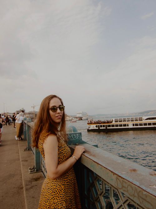 Free Woman in yellow dress on a bridge overlooking water, boats, and distant cityscape. Stock Photo