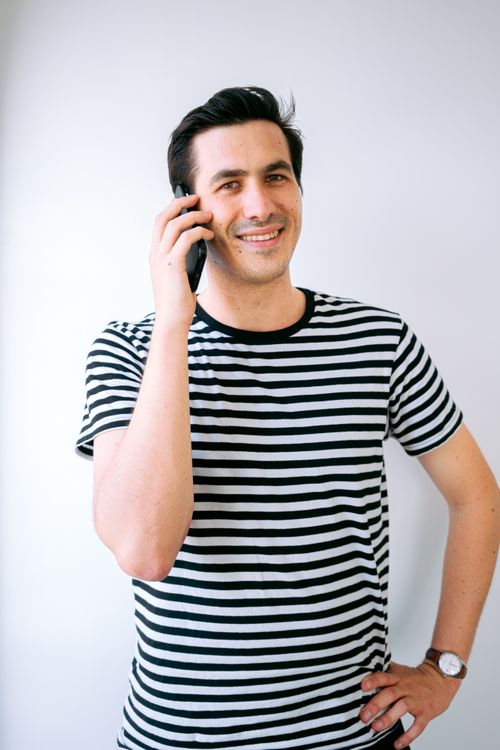Free Casual smiling man in striped shirt talking on mobile phone indoors against white background. Stock Photo