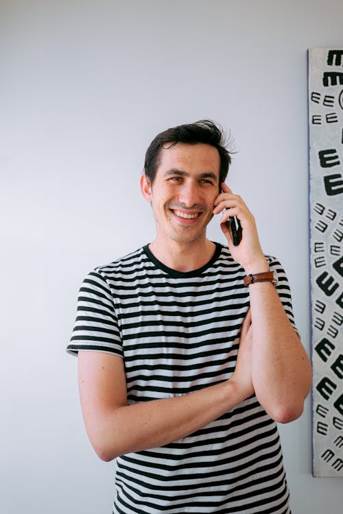 Man Holding Smartphone Standing Beside White Wall