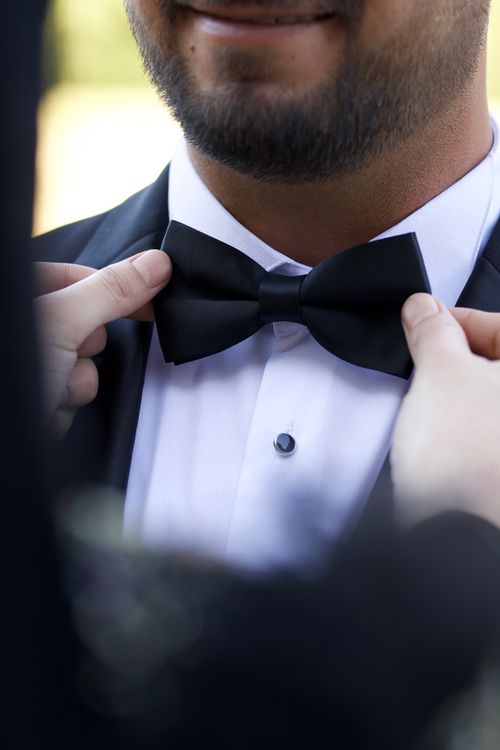 Free Close-up of a man adjusting his bow tie, dressed in a black tuxedo at a formal event. Stock Photo