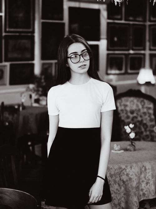 Free Black and white portrait of a young woman with glasses in a stylish indoor setting. Stock Photo