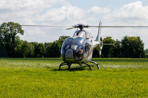 Free Helicopter resting on a green field under blue skies and scattered clouds. Stock Photo
