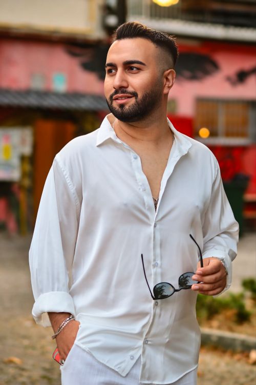 Free A confident man in a white shirt holds sunglasses, outdoors. Stock Photo