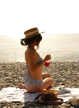 Woman enjoying a picnic on a pebble beach at sunset.