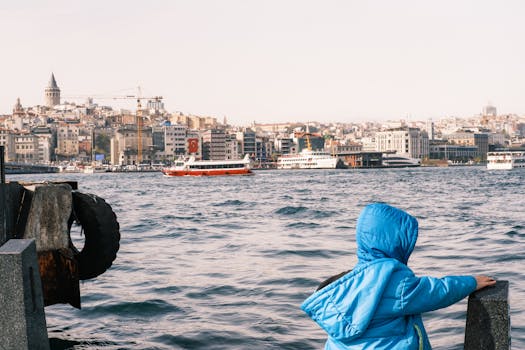 A child in a blue jacket gazes at the iconic Istanbul skyline with the Bosphorus in the foreground.