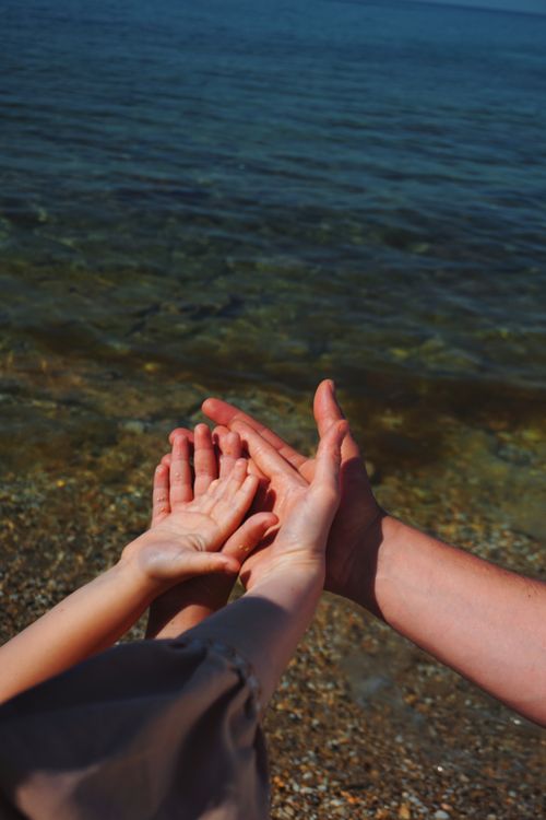Free Hands of child and adult reaching toward the calm sea on a sunny day, symbolizing connection. Stock Photo