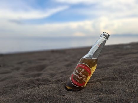 A bottled beer rests in the sand on a serene beach during twilight, highlighting relaxation and summer vibes.