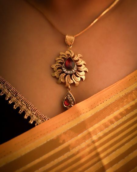 Sunburst gold pendant with a ruby-red centre worn on a fine chain