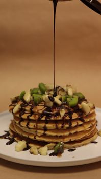 Mouthwatering pancakes topped with kiwi, banana, and chocolate sauce on a plate.