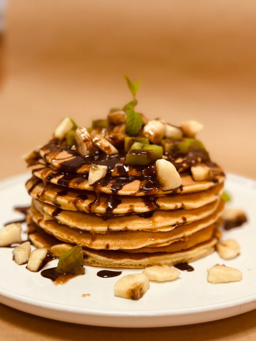 Free Stack of pancakes topped with banana, kiwi, and chocolate sauce on a white plate. Stock Photo