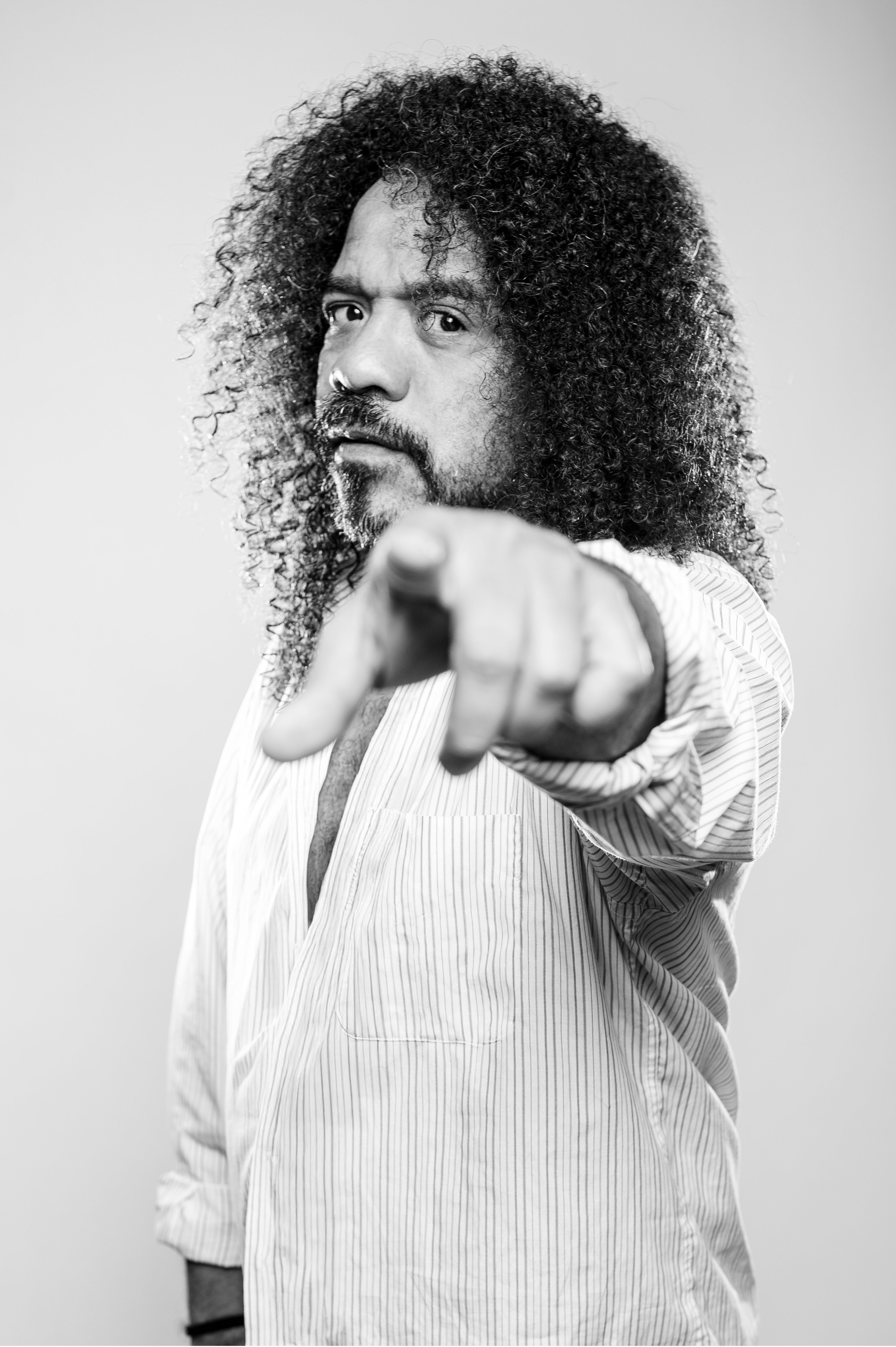 Black and white portrait of a man with curly hair pointing at the camera.
