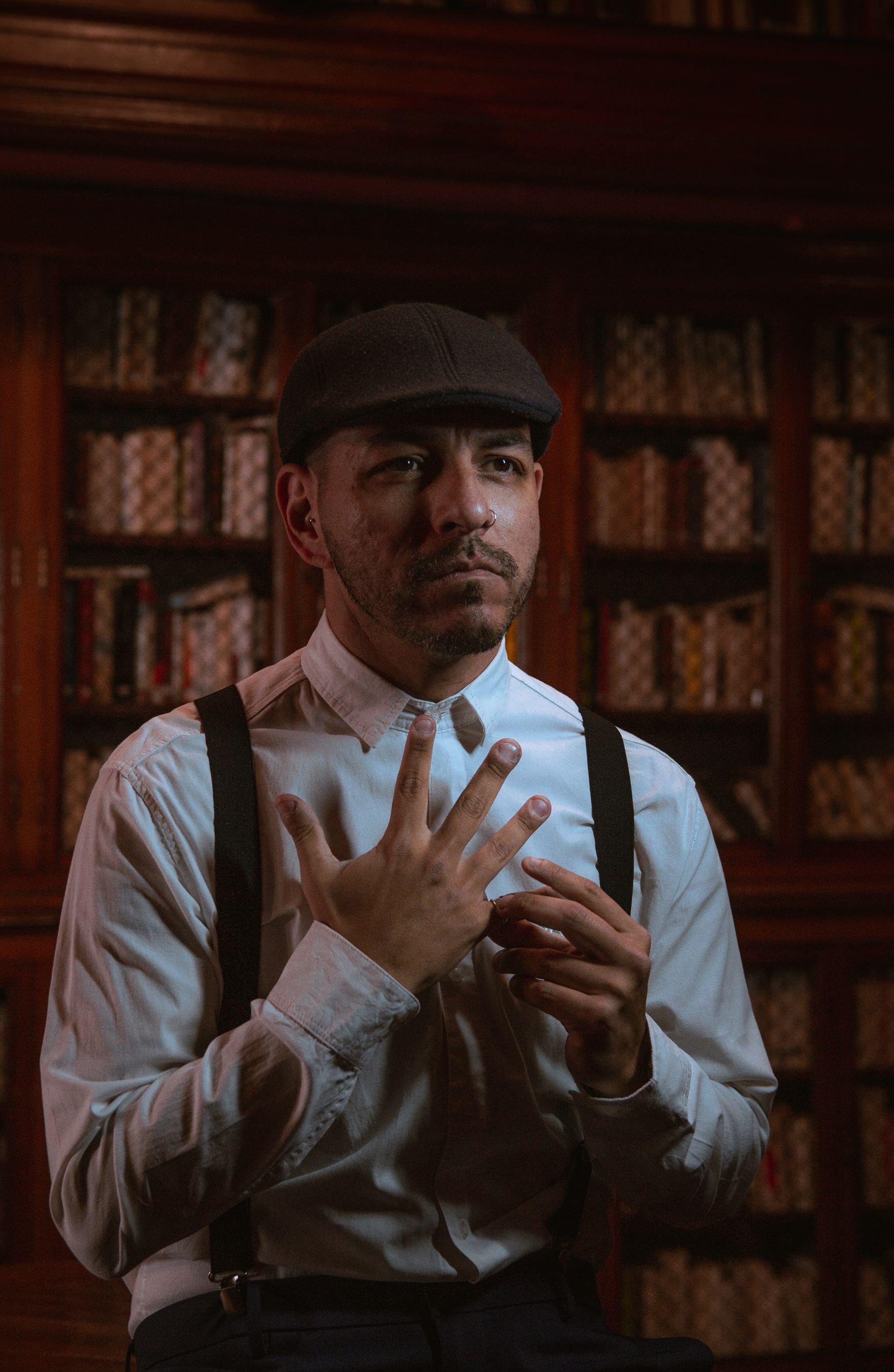 Portrait of a man with vintage style in a library setting, wearing suspenders and a flat cap.