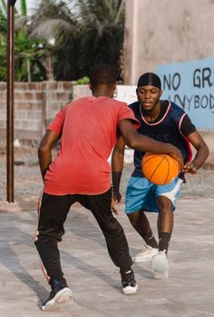 Two young men playing an intense game of basketball outdoors.