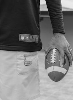 Monochrome photo of an individual holding a football, wearing casual attire outdoors.