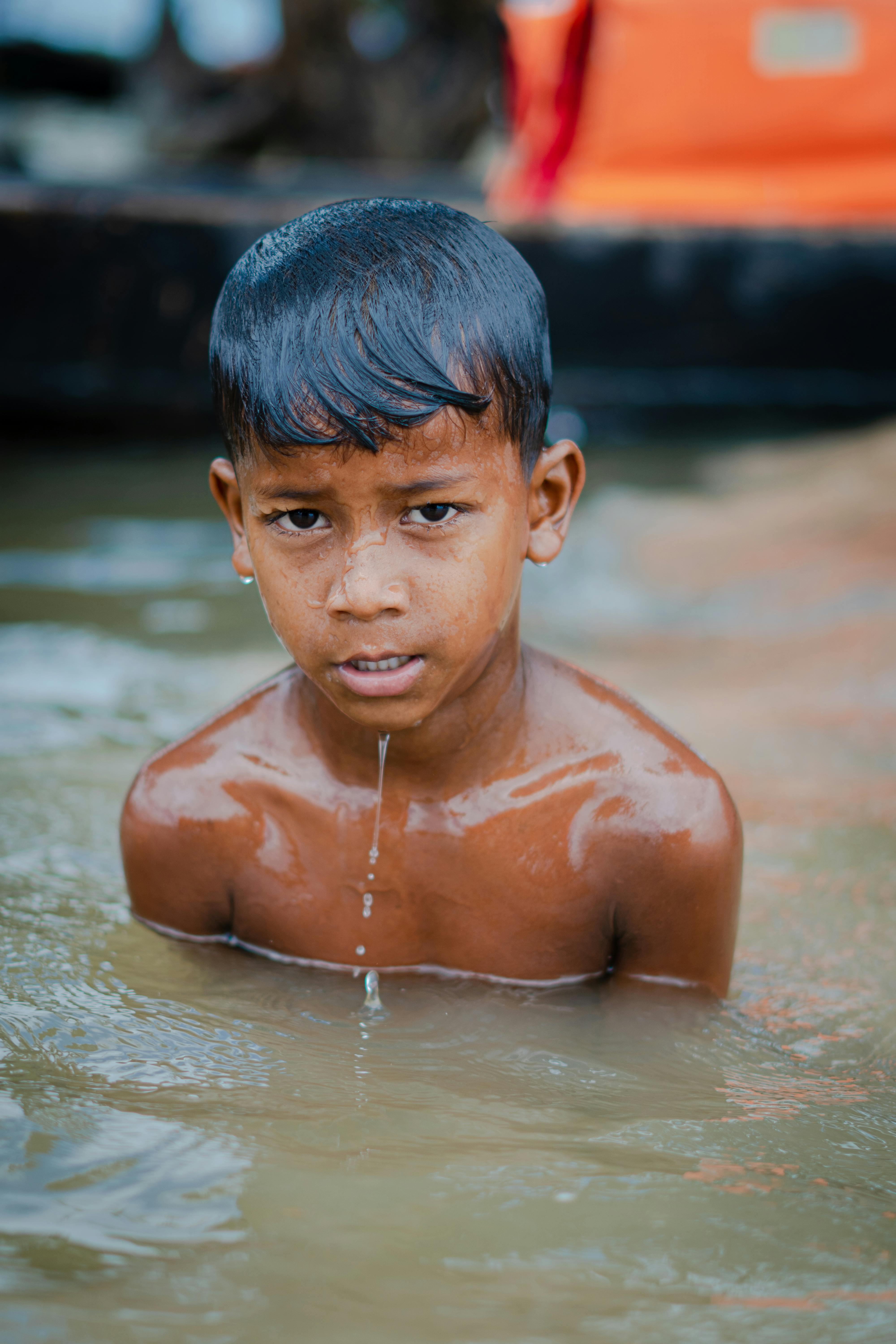 A young boy is swimming in water with a determined expression, droplets running down his face.