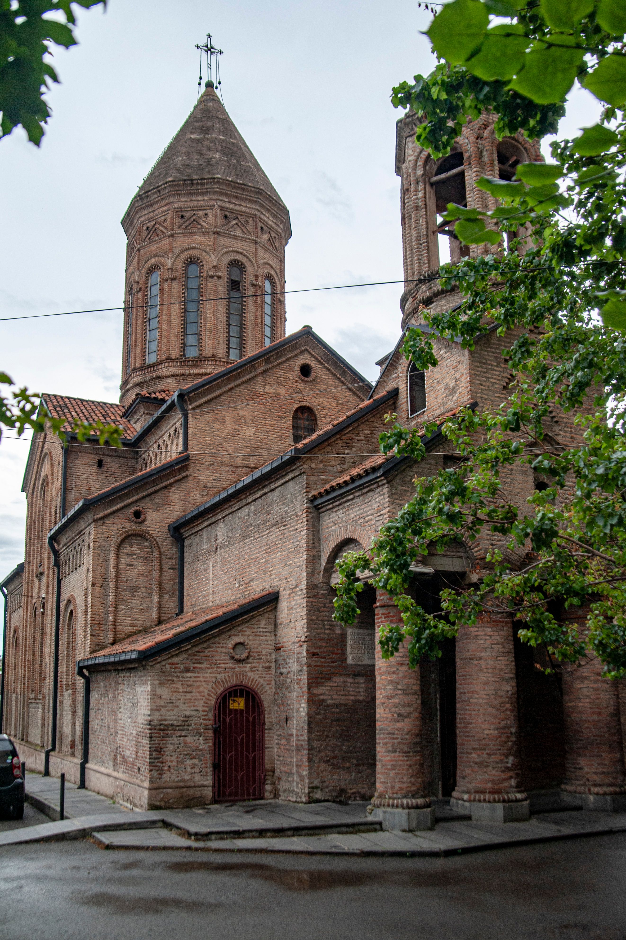 Capture of a historic brick Orthodox church with a distinctive dome and leafy foreground.