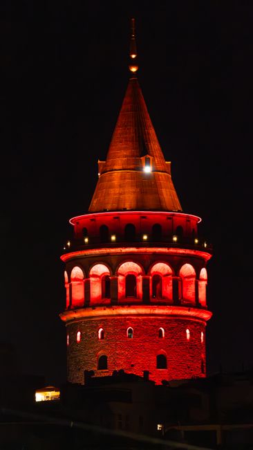 Striking night view of Galata Tower glowing red under the dark sky.
