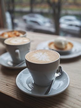 A close-up of cappuccino cups with latte art on a wooden table in a cozy cafe setting.